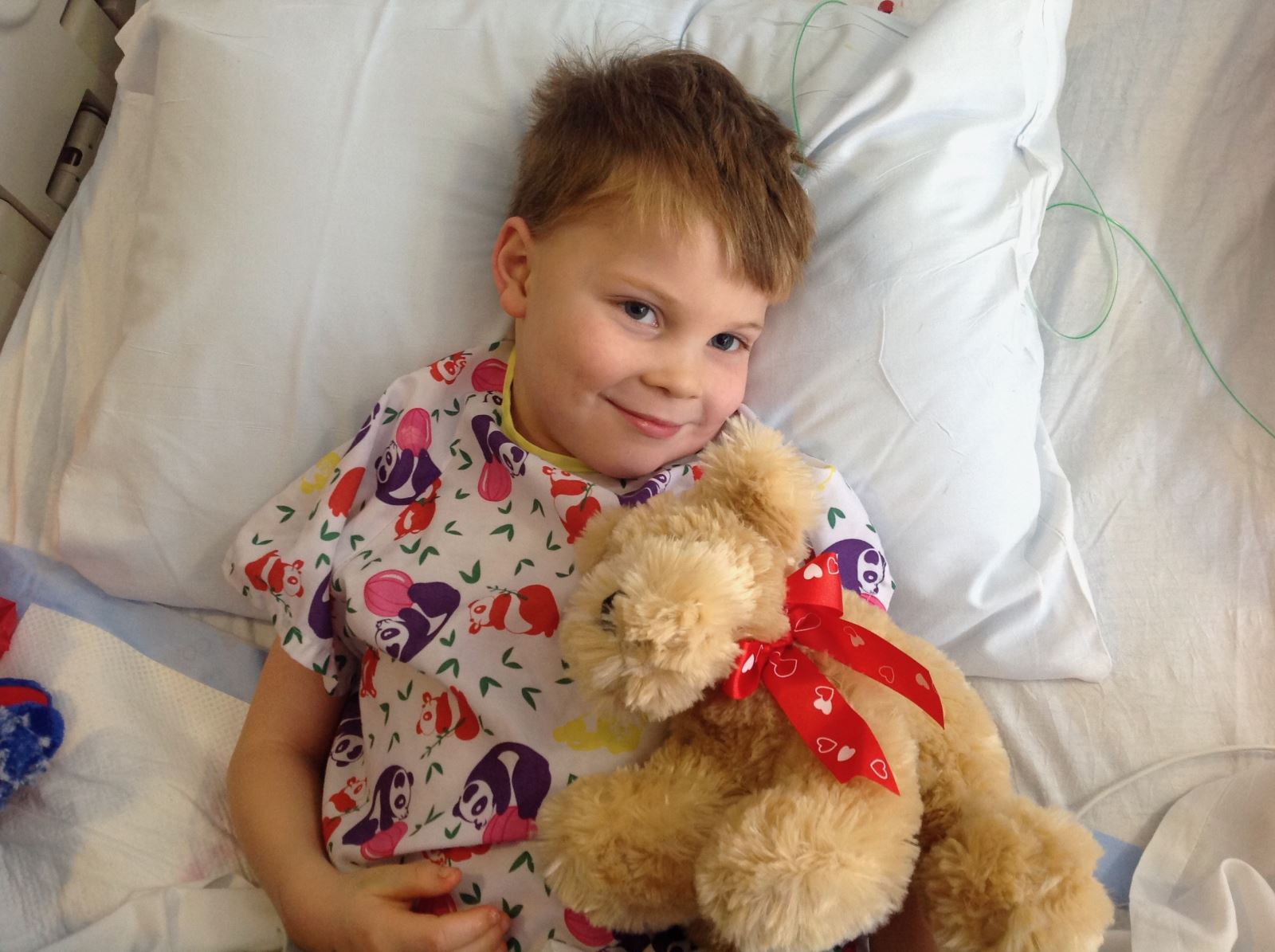 Young pediatric patient smiling while holding a teddy bear in hospital bed